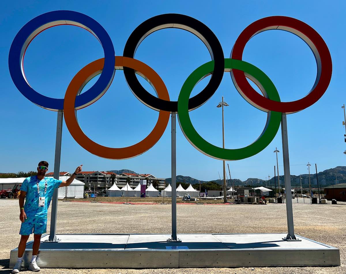 Ethan Westera staat bij de Olympische ringen van Marseille. 